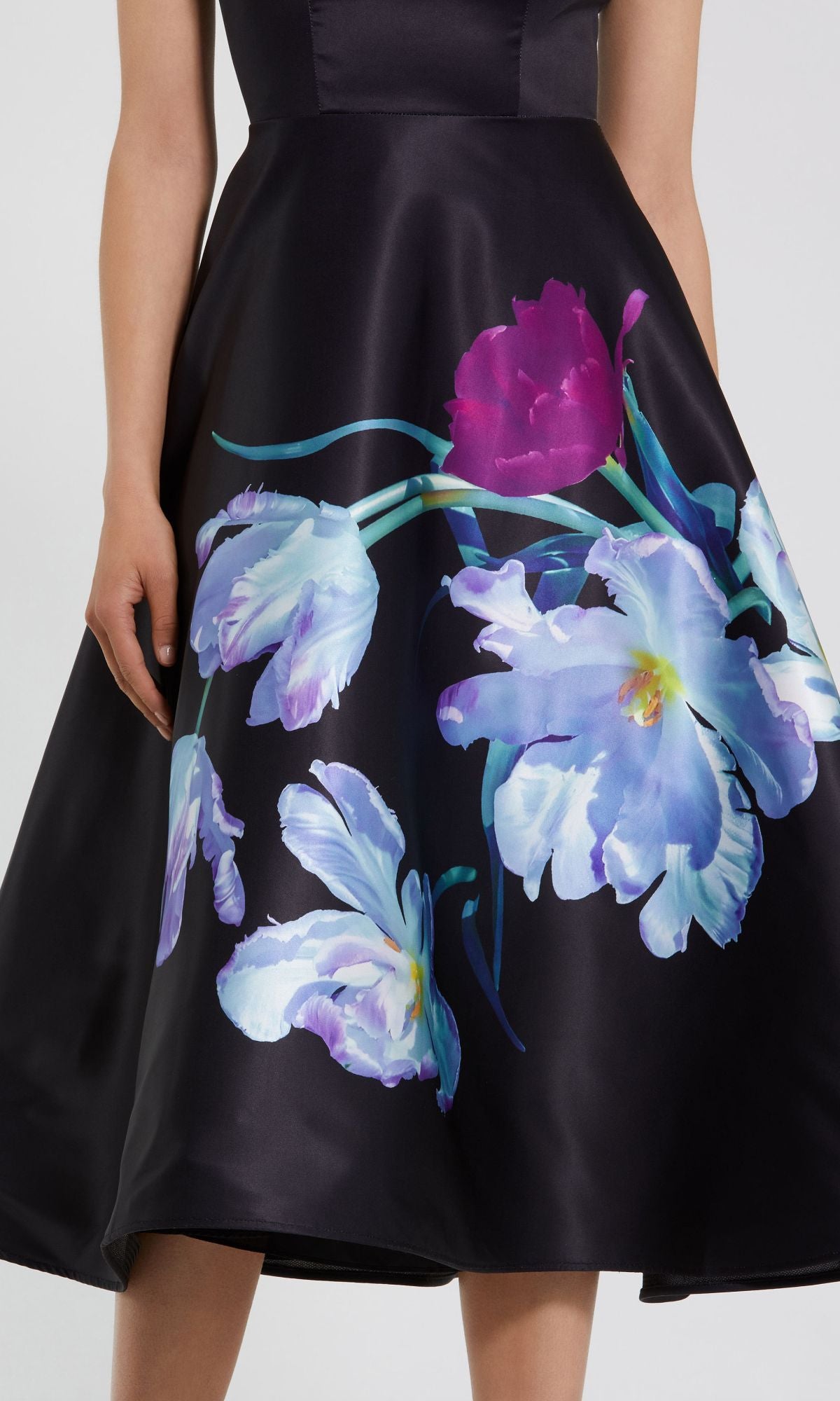 A woman in the Mac Duggal 20995 black satin wedding-guest dress featuring large, colorful purple, blue, and white floral prints on the skirt.